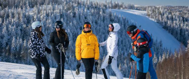 Grupp med skidåkare i vinterlandskap vid Hassela, med snöklädda träd och skidbacke i bakgrunden.